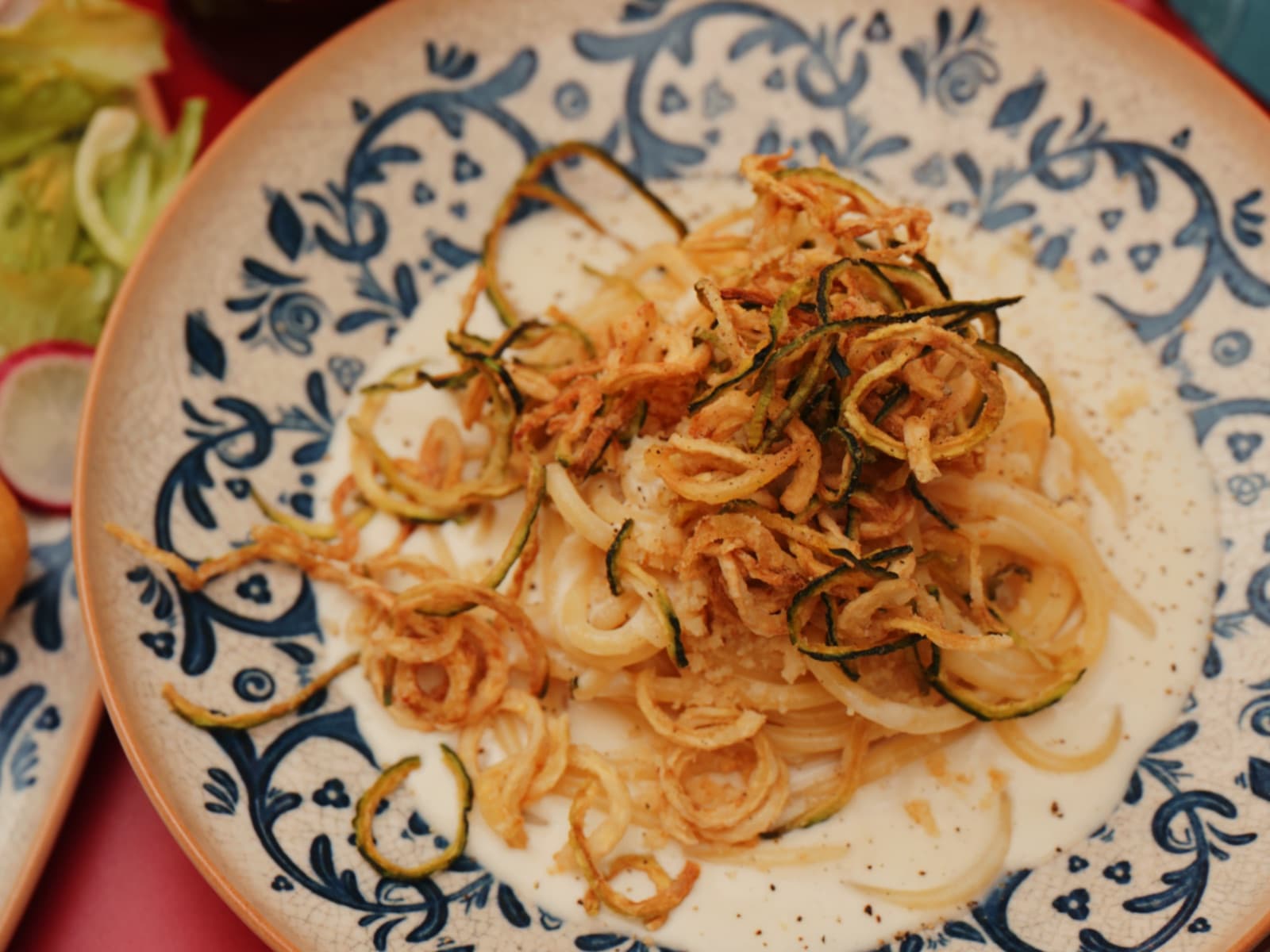 Pici-Pasta mit Pecorino und knusprigen Zucchini-Chips auf blau-weißem Keramikteller